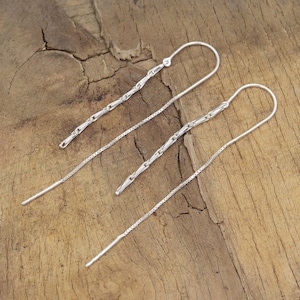 May include: A pair of silver chain earrings with a delicate, thin chain and a slightly thicker chain with a looped end.