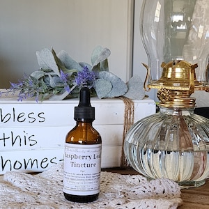 May include: A brown glass bottle with a dropper filled with Raspberry Leaf Tincture. The bottle is labeled with the text "Raspberry Leaf Tincture" and "For: Ease Labor & Delivery, Support, Soothes Symptoms, Blood Sugar Regulation, Support, Soothes Symptoms, Blood Sugar Regulation, 10 drops up to 3 times a day".