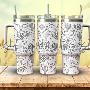 May include: Three white stainless steel tumblers with a black and white design featuring cactus, skulls, and geometric patterns. The tumblers have a gold lid and a handle.