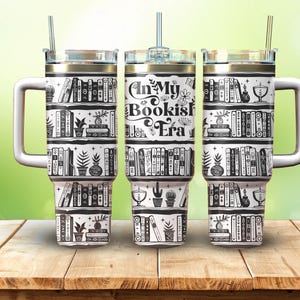 Puede incluir: Tres vasos de acero inoxidable con diseños en blanco y negro. Los vasos presentan un diseño de estantería con libros, plantas y el texto "In My Bookish Era".