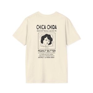 May include: A cream-coloured t-shirt featuring a graphic on the back. The design includes the text "CHICA-CHIDA" and "PEANUT BUTTER" alongside a stylized illustration of a woman's face. Additional text is also present.