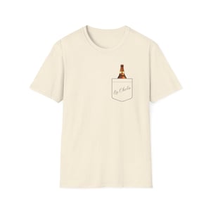Könnte beinhalten: Cremefarbenes T-Shirt mit einem Taschen-Design mit einer Bierflasche. Die Tasche hat den Text "La Chola" in handschriftlichem Stil. Die Bierflasche ist braun und goldfarben, und das Shirt hat einen klassischen Rundhalsausschnitt.