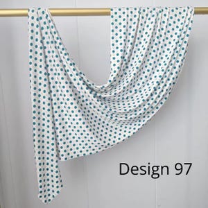 May include: A white fabric scarf featuring a repeating pattern of teal and light gray polka dots, draped over a gold rod. The fabric is labeled as Design 97, showcasing a soft, flowing texture with consistent circular motifs across the material.