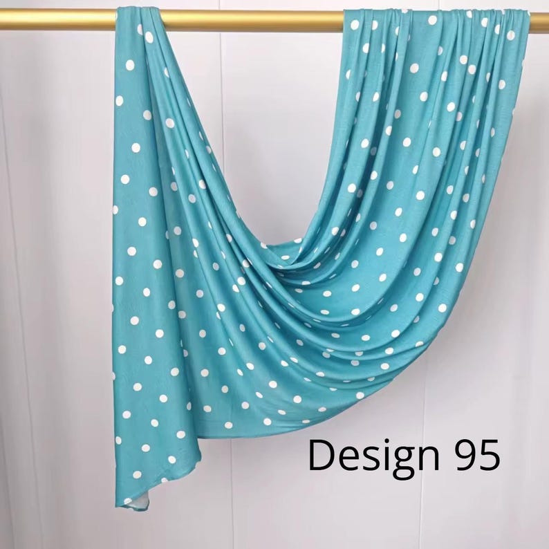 May include: A teal fabric scarf featuring a white polka dot pattern draped over a gold rod. The fabric hangs in soft folds, displaying a consistent print throughout. The text "Design 95" is printed in black in the lower right corner of the image.