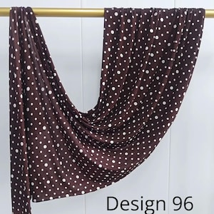 May include: A dark brown rectangular scarf featuring a repeating pattern of small white polka dots. The fabric is draped over a horizontal gold rod, creating soft folds and ripples. The text Design 96 is printed in black in the lower right corner.