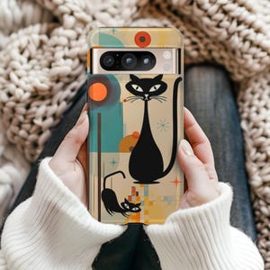 May include: A smartphone case featuring a graphic illustration of two black cats against a cream background with teal and orange circular shapes, thin vertical lines, and small starburst accents. The case has a horizontal camera cutout at the top.
