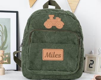 May include: A green corduroy backpack with a brown leather patch featuring a cartoon tractor and the name "Miles".