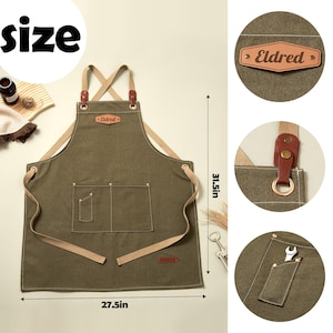 May include: An olive green apron with beige cross-back straps, a leather patch labeled Eldred, and multiple pockets. The apron measures 31.5 inches in height and 27.5 inches in width, featuring metal hardware and reinforced stitching details.