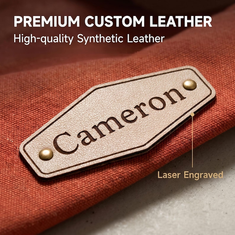 May include: A diamond-shaped beige synthetic leather patch with the laser-engraved name Cameron, secured by two brass-colored metal rivets onto a textured orange fabric. The text PREMIUM CUSTOM LEATHER, High-quality Synthetic Leather, and Laser Engraved appear.