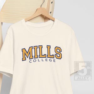 May include: A cream colored t-shirt with a navy blue and gold graphic that says "MILLS COLLEGE".