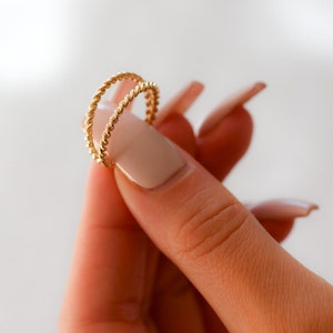 May include: A close-up of a gold, twisted, double band ring on a finger.