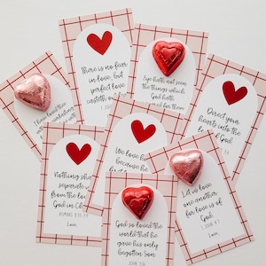 May include: A set of eight Valentine's Day cards with red and pink hearts and scripture verses about love. Each card has a small chocolate heart attached to it.