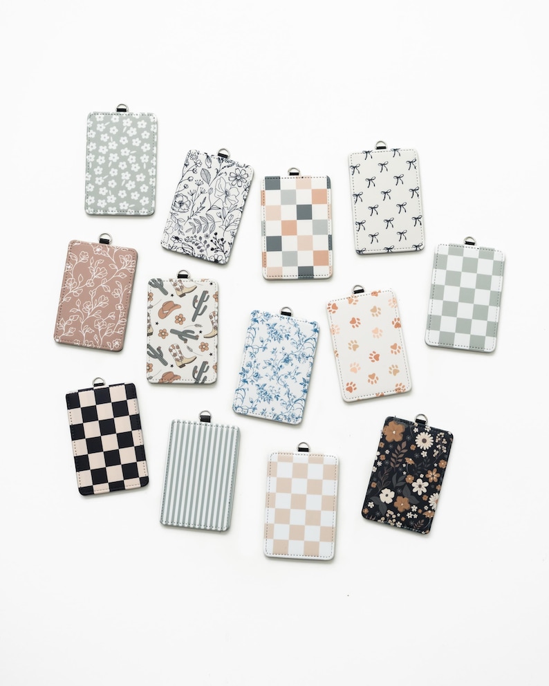 Puede incluir: Una colecci&oacute;n de tarjeteros rectangulares con varios dise&ntilde;os, incluyendo florales, a cuadros, a rayas y de lazo. La paleta de colores incluye blanco, negro, gris, rosa y azul. Cada tarjetero tiene un lazo met&aacute;lico plateado en la parte superior.