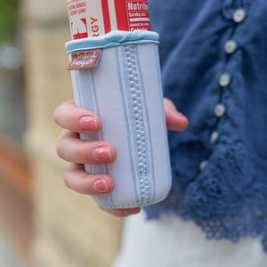 May include: A white and light blue striped beverage insulator with a light blue trim, holding a red and white can. The insulator has a brown tag that reads "Frederick Family Co."
