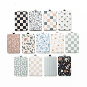 Puede incluir: Una colecci&oacute;n de tarjeteros rectangulares con varios dise&ntilde;os. Los dise&ntilde;os incluyen cuadros, flores, lazos, huellas de patas y rayas. Cada tarjetero tiene un lazo plateado en la parte superior.