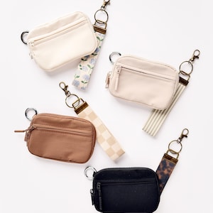 May include: An assortment of small, rectangular pouches in cream, tan, brown, and black. Each pouch has a zipper closure and a wrist strap with a metal clasp. The straps feature floral, checkered, striped, and animal print patterns.