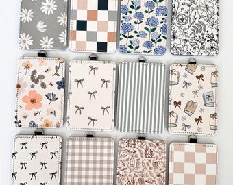 Könnte beinhalten: Eine Sammlung rechteckiger Ausweishalter mit verschiedenen Mustern. Designs umfassen Gänseblümchen, Schachbrettmuster, Blumendrucke, Schleifen, Streifen und einen Wüsten-Themen-Druck. Jeder Halter hat eine silberfarbene Metallschlaufe oben.