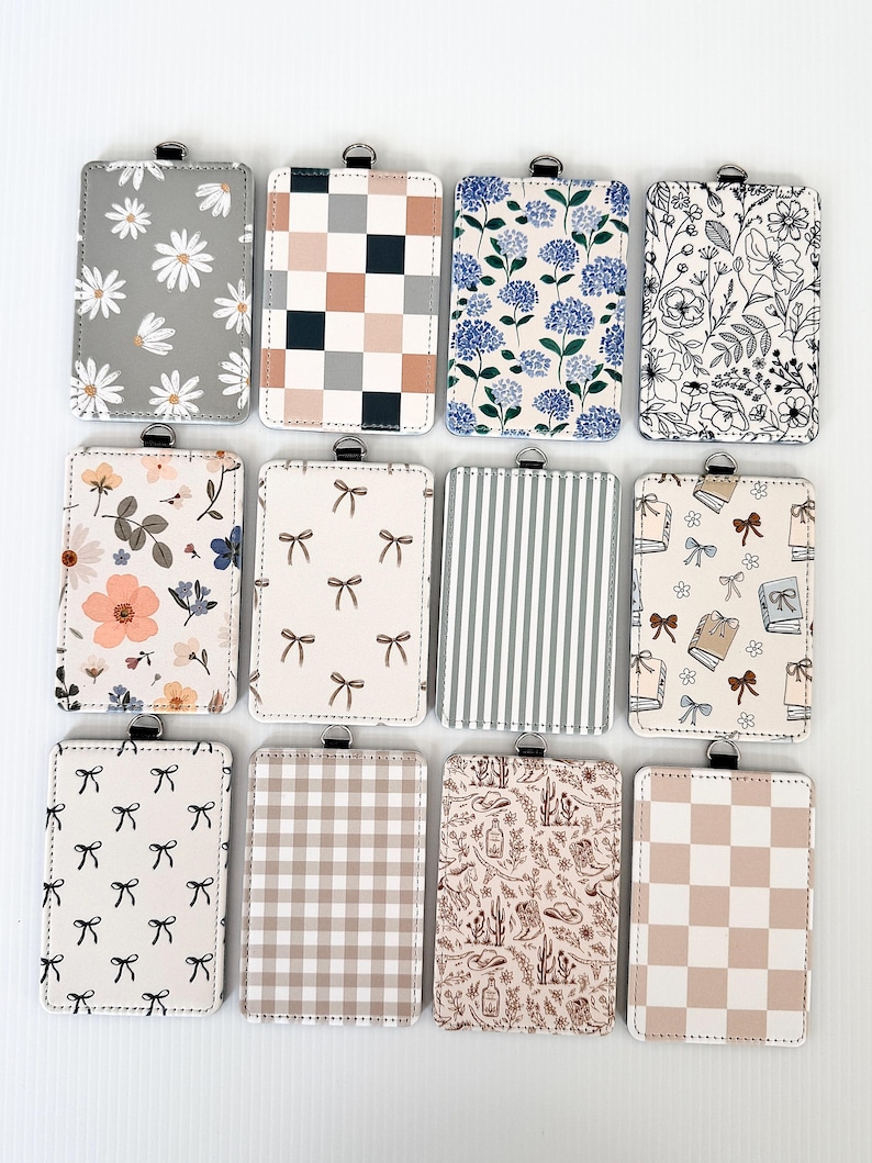 Puede incluir: Una colecci&oacute;n de porta-credenciales rectangulares con varios dise&ntilde;os. Los dise&ntilde;os incluyen margaritas, patrones de cuadros, estampados florales, lazos, rayas y un estampado tem&aacute;tico del desierto. Cada porta-credencial tiene un lazo met&aacute;lico plateado en la parte superior.