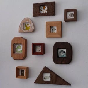 May include: A selection of small wooden framed artworks, each with a watercolour illustration of an animal. The frames vary in shape and wood tone, including a tiger, a monkey, a mouse, a bear, a seal, a fox, a hedgehog, a dinosaur, and a seal.