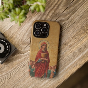 May include: A gold iPhone case featuring a religious image of a woman in red robes holding a chalice. The woman is surrounded by children. The case has a textured surface.