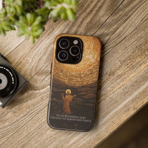 Op de afbeelding: Een zwarte telefoonhoes met een gouden en bruine afbeelding van een man met uitgestrekte armen. De tekst "In the beginning God created the heaven and earth" staat onderaan de hoes gedrukt.