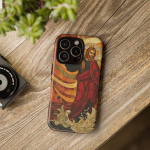 May include: A phone case with a mosaic design featuring a religious figure in a red robe. The figure is standing on a wave with a golden halo above their head.
