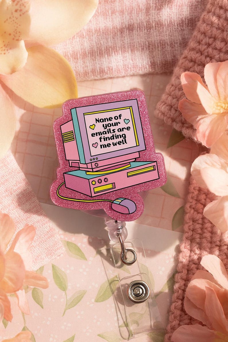 Puede incluir: Un portatarjetas en forma de ordenador rosa y morado con el texto "None of your emails are finding me well". El portatarjetas tiene un cord&oacute;n retr&aacute;ctil y un clip de pl&aacute;stico transparente. El dise&ntilde;o incluye un monitor de ordenador, una base de ordenador y un rat&oacute;n.