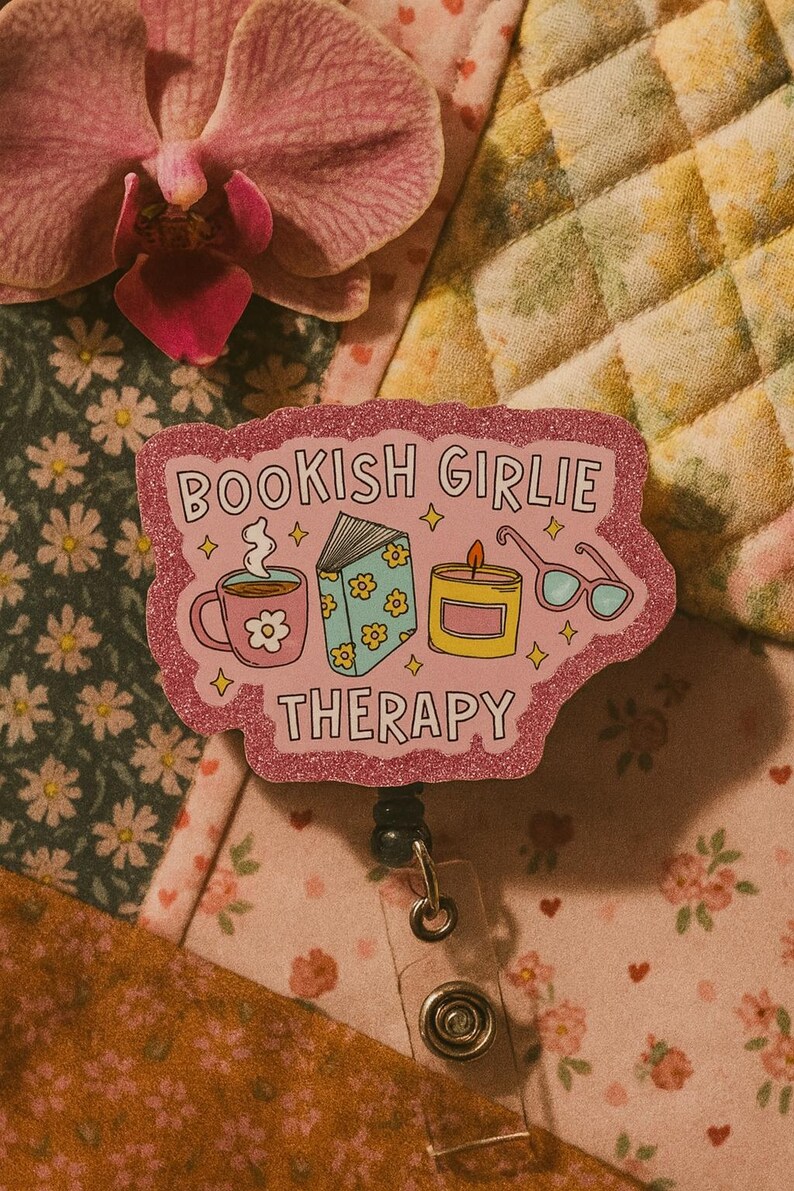 Puede incluir: Una insignia rosa brillante con las palabras "BOOKISH GIRLIE THERAPY" e ilustraciones de una taza, un libro, una vela y gafas. La insignia est&aacute; sobre un fondo floral con una flor rosa.