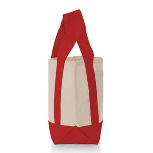 May include: A canvas tote bag with a rectangular shape. The bag features a cream-colored body with red accents on the bottom and handles. The handles are long and extend from the bottom to the top of the bag.