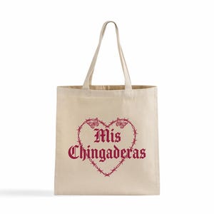 K&ouml;nnte beinhalten: Beige Canvas-Tragetasche mit einem bordeauxroten herzf&ouml;rmigen Design. Das Herz besteht aus Stacheldraht und Schmetterlingen, mit den Worten "Mis Chingaderas" in einer gotischen Schrift.