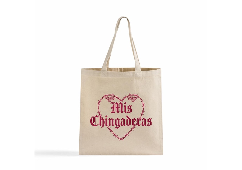 K&ouml;nnte beinhalten: Beige Canvas-Tragetasche mit einem bordeauxroten herzf&ouml;rmigen Design. Das Herz besteht aus Stacheldraht und Schmetterlingen, mit den Worten "Mis Chingaderas" in einer gotischen Schrift.