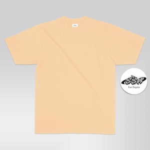 May include: A solid light peach-coloured short-sleeve t-shirt with a crew neckline. A small white circular graphic is positioned to the right, featuring the black text SSA and Los Angeles in a stylised font inside a black oval shape.