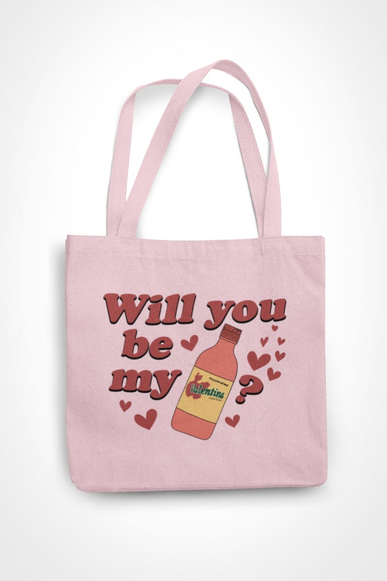 Op de afbeelding: Roze draagtas met de tekst "Will you be my" en een fles Valentina-chilisaus. Het ontwerp bevat rode harten en een vraagteken. De tas heeft twee roze handvatten.