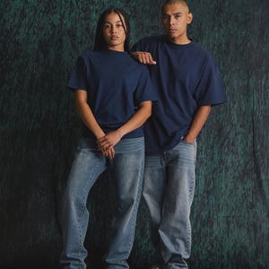May include: Two individuals wearing matching navy blue short-sleeved crew neck t-shirts paired with light blue denim jeans. The t-shirts feature a solid colour design with a standard fit, while the jeans have a relaxed cut and a classic wash.
