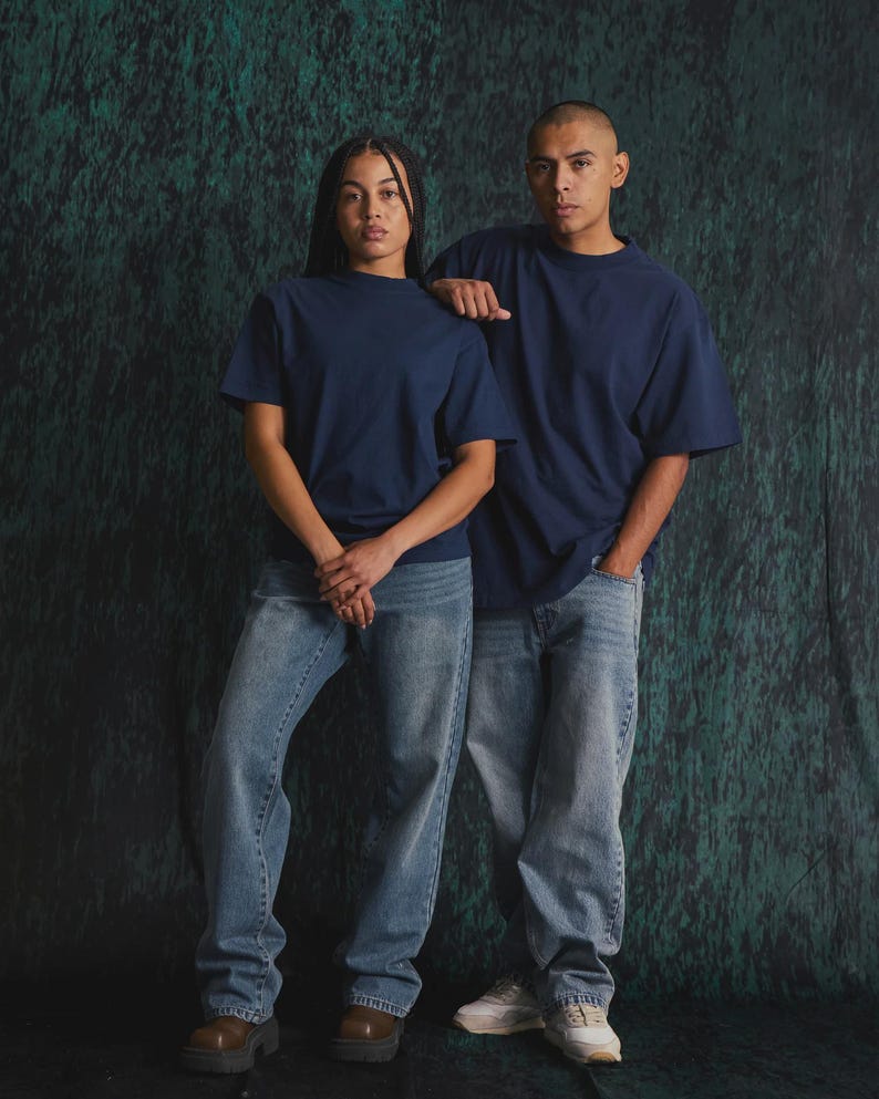 May include: Two individuals wearing matching navy blue short-sleeved crew neck t-shirts paired with light blue denim jeans. The t-shirts feature a solid colour design with a standard fit, while the jeans have a relaxed cut and a classic wash.
