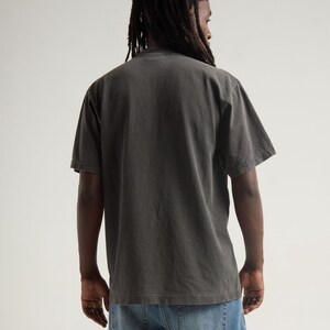 May include: A short-sleeved, charcoal grey t-shirt with a crew neckline, worn with blue denim jeans. The shirt features a solid, plain back design with a relaxed fit, showcasing a faded, washed-out fabric texture and standard hemline construction.