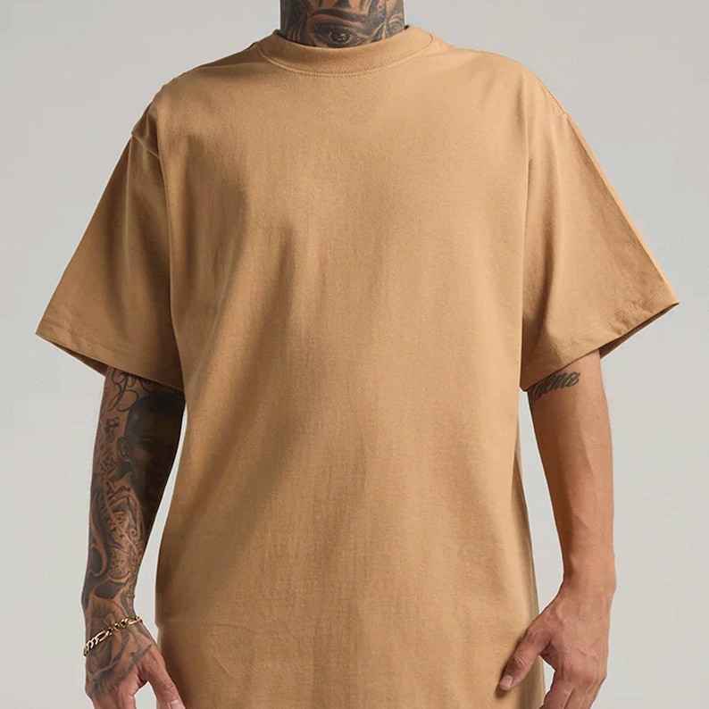 May include: A solid tan short-sleeve t-shirt with a crew neckline. The garment features a relaxed fit with wide sleeves and a plain, unpatterned fabric construction. The shirt is presented in a simple, straightforward style without any additional graphics or text.