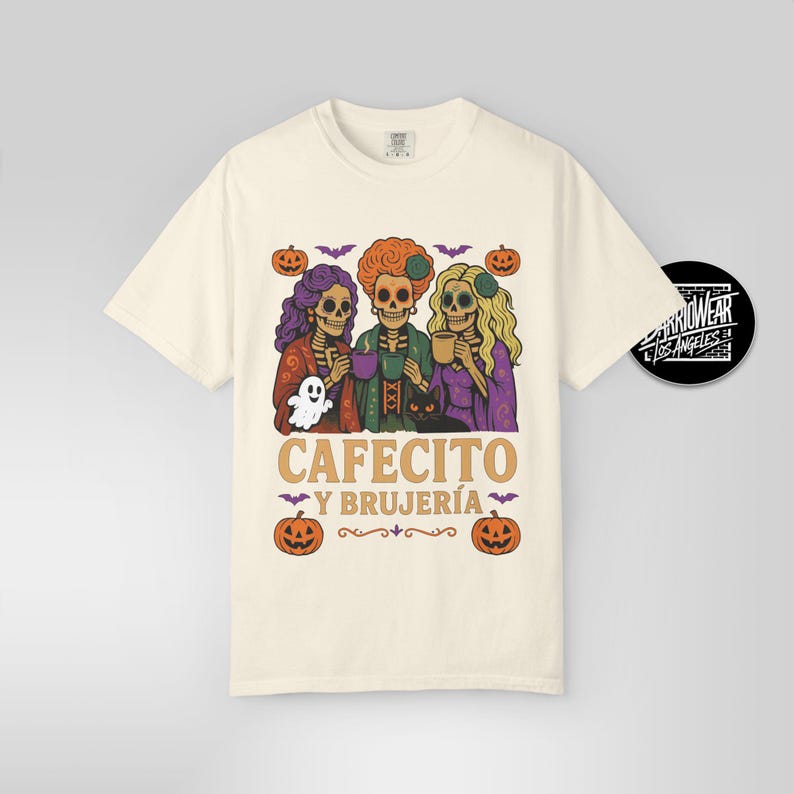 May include: Cream-colored t-shirt featuring a Halloween-themed graphic. The design includes three skeleton figures with colorful hair, holding cups and a ghost. The text "CAFECITO Y BRUJER&Iacute;A" is printed below the figures, with pumpkins and bats.