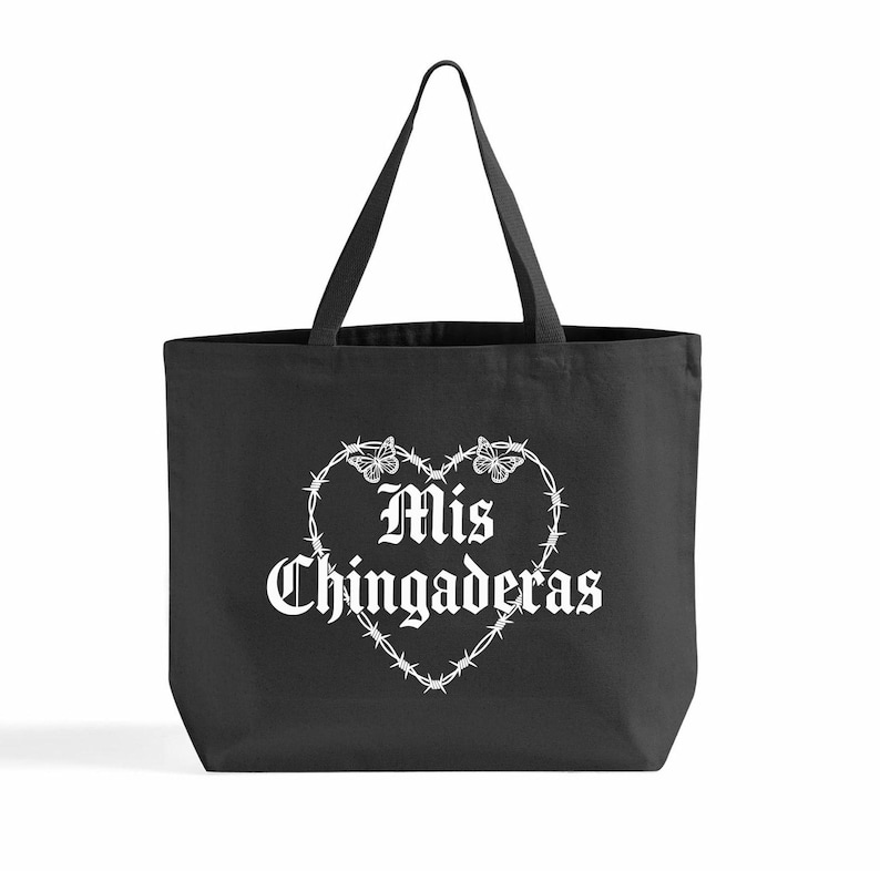 K&ouml;nnte beinhalten: Schwarze Tragetasche mit wei&szlig;em Text "Mis Chingaderas" in einem herzf&ouml;rmigen Stacheldrahtdesign. Zwei Schmetterlinge befinden sich oben auf dem Herzen. Die Tasche hat zwei schwarze Griffe.
