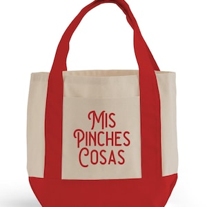 K&ouml;nnte beinhalten: Eine Canvas-Tragetasche mit cremefarbenem Korpus, rotem Boden und roten Griffen. Auf der Vorderseite der Tasche steht der Schriftzug "Mis Pinches Cosas" in roter Schrift. Die Tasche hat eine einfache Tasche auf der Vorderseite.