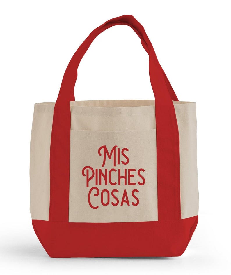 K&ouml;nnte beinhalten: Eine Canvas-Tragetasche mit cremefarbenem Korpus, rotem Boden und roten Griffen. Auf der Vorderseite der Tasche steht der Schriftzug "Mis Pinches Cosas" in roter Schrift. Die Tasche hat eine einfache Tasche auf der Vorderseite.