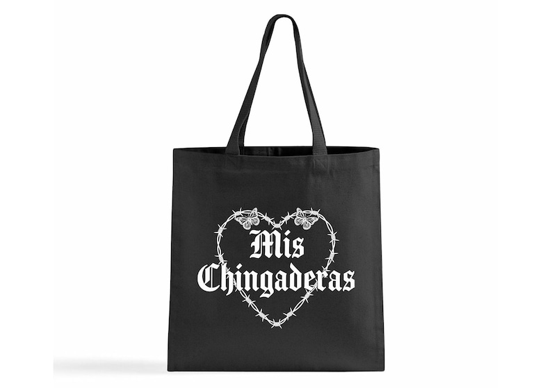K&ouml;nnte beinhalten: Schwarze Tragetasche mit wei&szlig;em Text und einem herzf&ouml;rmigen Design. Das Herz wird von Stacheldraht gebildet und tr&auml;gt die Worte "Mis Chingaderas" in gotischer Schrift mit Schmetterlingsakzenten.