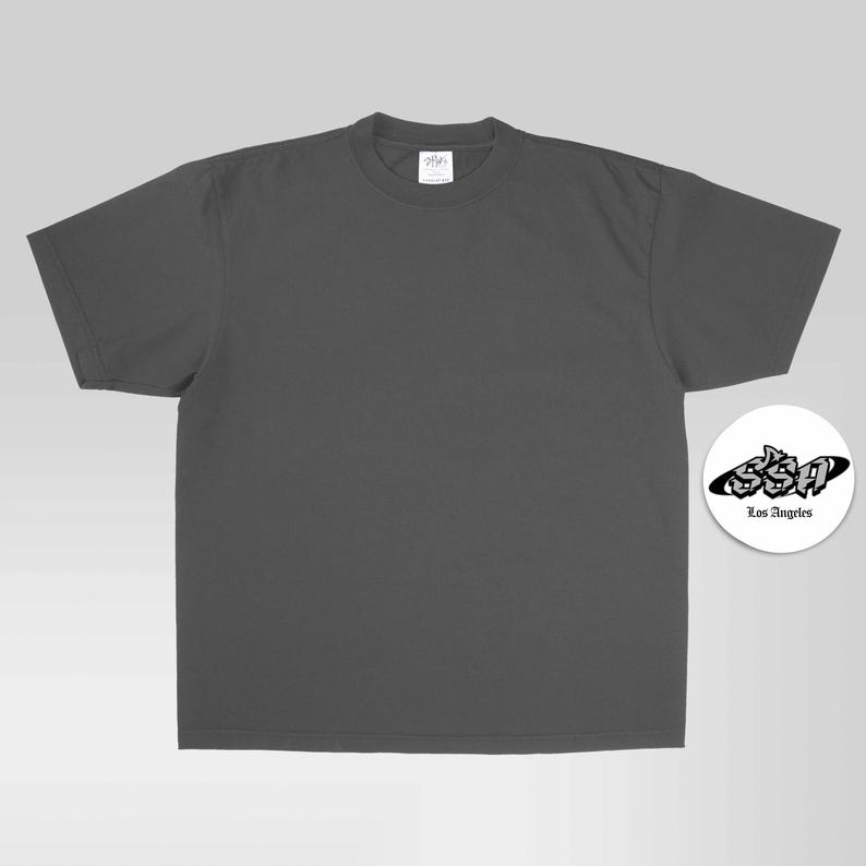 May include: A charcoal gray short-sleeve t-shirt with a crew neckline. To the right, a circular white emblem features the black text SSA in a stylized graffiti font, with the words Los Angeles printed in a smaller, simple black font underneath.