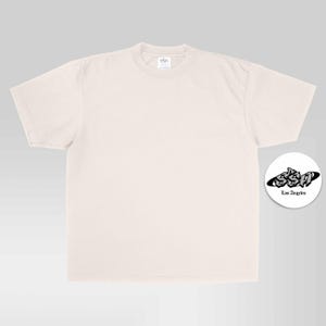 May include: A plain, light beige short-sleeve t-shirt with a crew neckline. To the right, a circular white sticker features the black text SSA in a stylized graffiti font, with the words Los Angeles printed in a smaller, simple font below it.