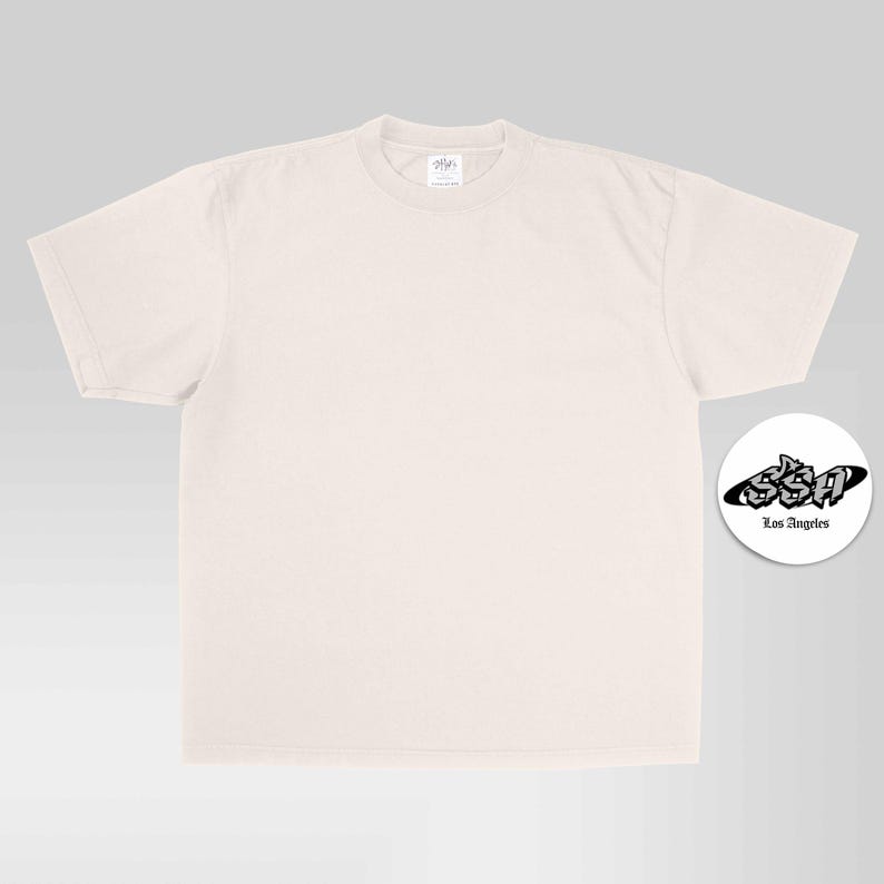May include: A plain, light beige short-sleeve t-shirt with a crew neckline. To the right, a circular white sticker features the black text SSA in a stylized graffiti font, with the words Los Angeles printed in a smaller, simple font below it.