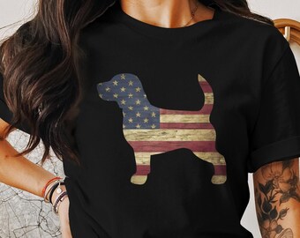 Op de afbeelding: Zwart T-shirt met een silhouet van een hond in de vorm van de Amerikaanse vlag. De hond is rood, wit en blauw met een houtnerf.