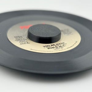 May include: A black vinyl record with a black center label. The label has white text that reads "You Be Illin'" and "Run-D.M.C."