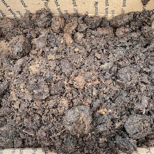 May include: A close-up of dark brown soil, likely compost, filling a cardboard box. The box is printed with the text "Priority Mail" and "Thank you for using Priority Mail".