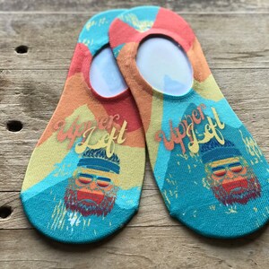 May include: A pair of colorful no-show socks with a mountain scene and the text "Upper Left" printed on them. The socks feature a cartoon character with a beard and sunglasses.