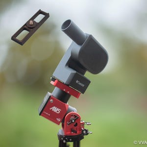 May include: A red and black telescope mount with a gray camera attached. The mount has a label that says "AMS" and "X-INR." The camera has a label that says "Celestron".
